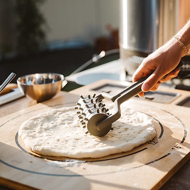 Person using a pizza docker on a pizza dough on a wooden board.