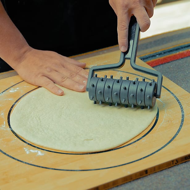 Person using a pizza dough roller on a wooden board with a textured surface.
