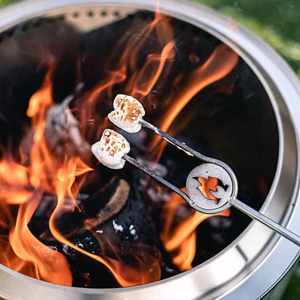 Marshmallows being roasted over a campfire using a metal skewer with a fire pit in the background.