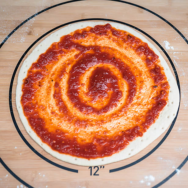 Unbaked pizza with tomato sauce spread in a spiral on a wooden board.